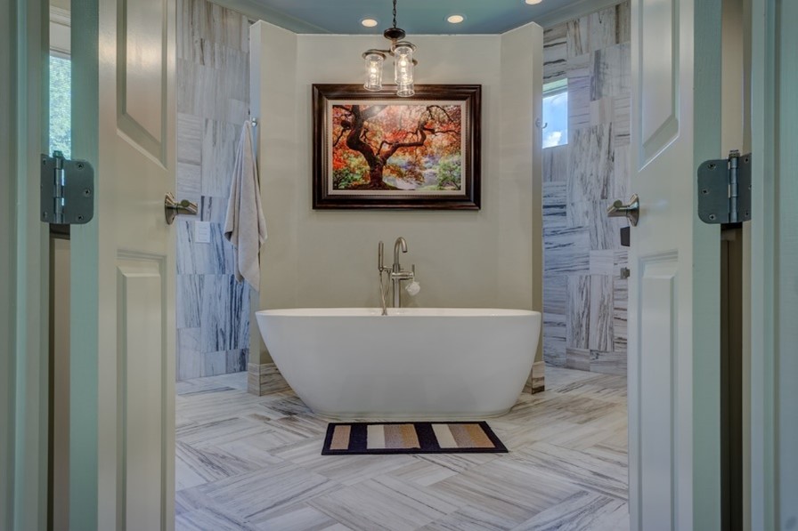 Image of double doors opening to a marble-walled and marble-floored bathroom featuring a white freestanding soaking tub.